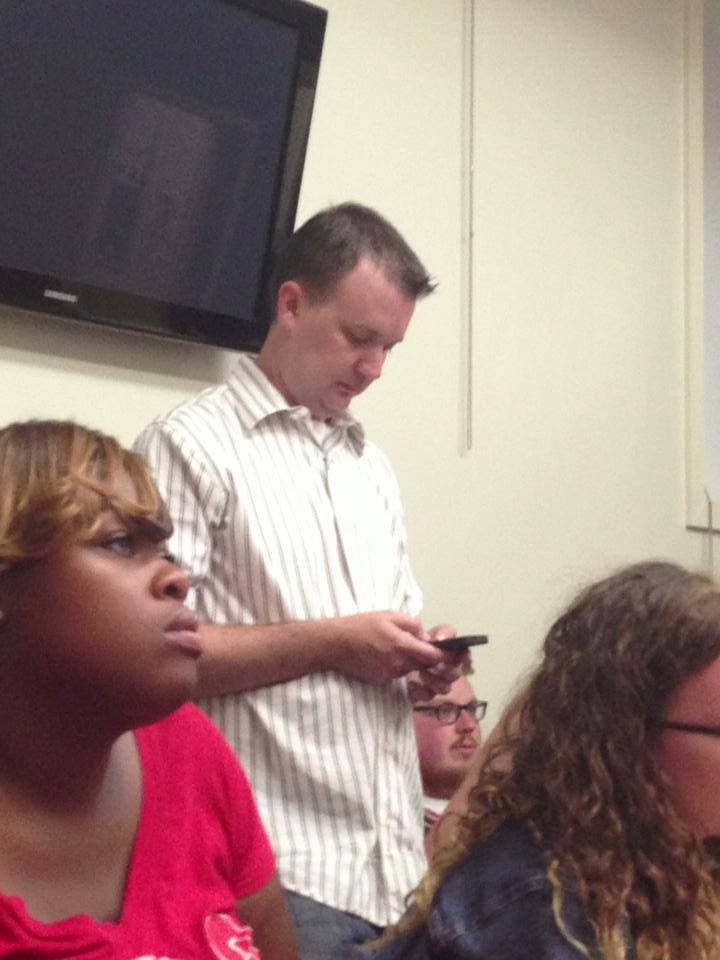 WVCW adjunct professor Jon standing in the classroom staring at his phone
